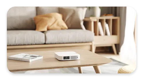 small portable Android DLP projector sitting flush on a coffee table projecting to a nearby wall. Showcasing how small android projectors have come.