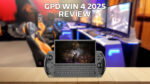 An image of the GPD WIN 4 2025 model showcasing its compact handheld gaming device with a physical keyboard and integrated gaming controls The device is displayed against a wooden surface in the foreground with a blurred gaming setup featuring multiple monitors and gaming chairs in the background The text GPD WIN 4 2025 REVIEW is prominently placed at the top of the image