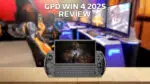 An image of the GPD WIN 4 2025 model showcasing its compact handheld gaming device with a physical keyboard and integrated gaming controls The device is displayed against a wooden surface in the foreground with a blurred gaming setup featuring multiple monitors and gaming chairs in the background The text GPD WIN 4 2025 REVIEW is prominently placed at the top of the image
