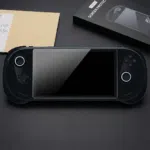 A black AYANEO 3 handheld gaming console lies centered on a dark surface, featuring a newly applied tempered glass screen protector. The console's dual joysticks are illuminated with circular white LED rings. To the top right, the product packaging is visible, showing a black box labeled "METIK SCREEN PROTECTOR" with an illustrative diagram of the installation process. The sleek, matte black finish of the device and the glossy reflection on the protected screen create a high-end, tech-focused aesthetic.