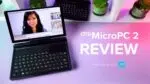 A dynamic thumbnail for a GPD MicroPC 2 review video A black GPD MicroPC 2 is prominently featured in the foreground open and angled towards the viewer with its screen displaying a video conference call featuring a womans face The laptops compact keyboard and trackpad are visible The background is a white shelf with potted plants and another GPD MicroPC 2 The desk below the laptop is a vibrant pink and purple gradient Large white text to the right of the laptop reads GPD MicroPC 2 REVIEW and smaller text below that says Intel N250 vs N300 alongside the Intel inside logo