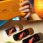 A split view image showing the KONKR Pocket Fit The top half is a close up of a hand holding the back of the yellow console highlighting the speaker grille The bottom half shows a top down view of the white yellow and black consoles arranged on a wooden table each with a glowing orange abstract design on its screen The white and black consoles feature illuminated joysticks