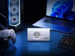 A lifestyle shot of the white SSD reader placed centrally on a blue-lit desk setup, flanked by a gaming PC tower, a game controller, and a laptop.