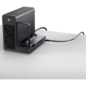 Black desktop NAS/enclosure with a pull-out drive bay and front hexagonal vent, power button, and a cable connected on a white desk surface.